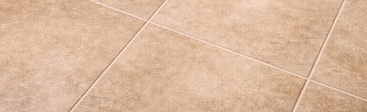 Close-up texture of beige ceramic tile kitchen flooring with subtle natural stone pattern and light grout lines, realistic material surface detail.